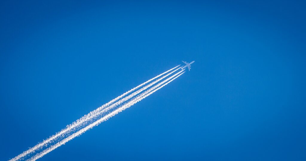 Airplane flying in the blue sky with contrails behind it
